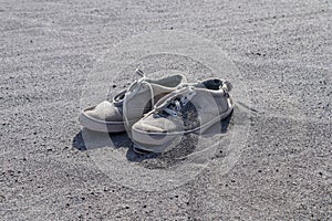 Old torn white sneakers on black volcanic sand. A pair of tie shoes with laces in volcanic ash. Discarded destroyed shoes