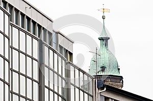 Old tower of a church behind the ugly glass faÃ§ade of a new building