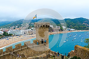 Old tower and stone fortress walls against background of resort town of Tossa de Mar, Spain