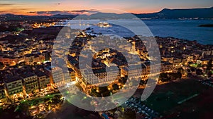 Old town with illumination against background of red sunset sky in Kerkyra, Corfu island. Evening aerial sunset view of