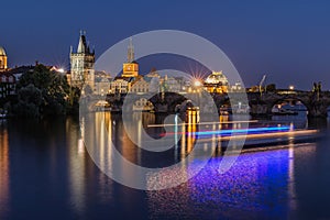 Charles Bridge and Old Town Tower at night with reflections on the Vltava and light from the boat
