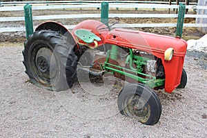 An old tractor colored green and red with flat rear tires on a farm parked in gravel next to a fence