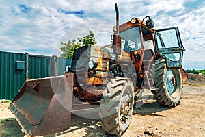 Old tractor. Low angle of rusty agricultural machine with huge wheels parked on village street near farm fence barn