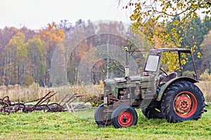 Old tractor with old agricultural tools on a meadow in an autumn landscape