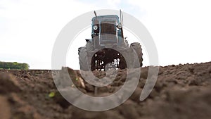 Old tractor plowing field, preparing land for sowing, driving over the camera at sunset, bottom