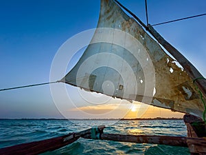 Old traditional maritime traditional vessel Dhow boat sailing under torned sail in the open Indian ocean near Zanzibar island in