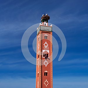 Old traditional terracotta minaret with storks nest on the top and arabic man painting ornament from the window. Morocco