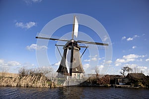 Old, traditional windmill in the Dutch canals. Netherlands.White clouds on a blue sky, the wind is blowing.
