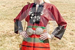 Old traditional women`s clothing. A young girl - a woman in Bulgarian folk costume. Silver ornaments, red robe and silver belt.