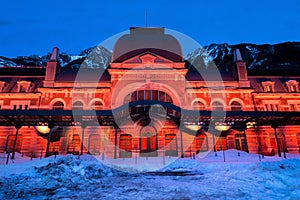 Old train station of Canfranc with the facade illuminated in reddish tones on a winter night with snow on the tracks, Huesca,