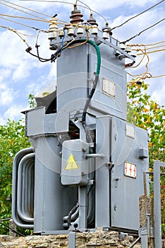 An old transformer substation for the distribution and transmission of electricity stands in the middle of a garden against a blue