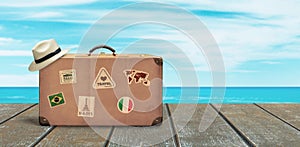 Old travel suitcase and white hat on wooden floor with sea and sky in background