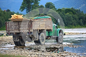 Old truck transports cargo wade across the river