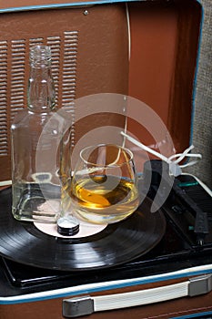 Old turntable. Nearby is a glass of strong alcohol and an empty glass bottle. Retro party equipment