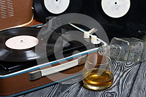 Old turntable. Nearby is a glass of strong alcohol and an empty glass bottle. Retro party equipment