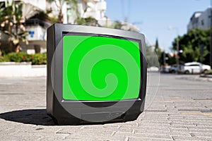 Old TV set with a green screen on the city street with cars