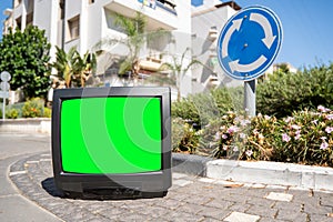 Old TV set with a green screen on the city street with cars