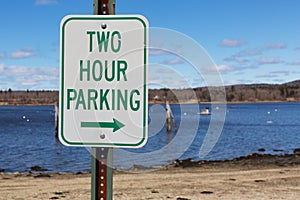 Old two hour parking sign with a right arrow in front of a beach and ocean in the springtime in New England