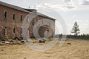 Old two-storied destroyed red house in autumn with sand around. Poverty and misery, North