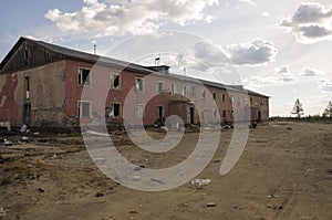 Old two-storied destroyed red house in autumn with sand around. Poverty and misery, North