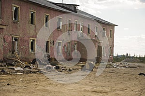 Old two-storied destroyed red house in autumn with sand around. Poverty and misery, North