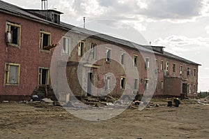 Old two-storied destroyed red house in autumn with sand around. Poverty and misery, North