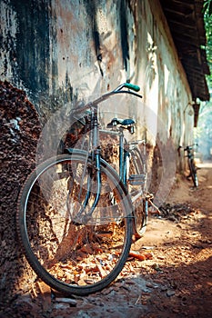 Old two-wheeled bicycle against a wall in narrow alley in Gokarna, India. Dilapidated housing of poor residents. Conceptual