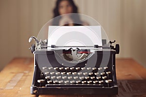 old typewriter in focus with person in background pondering, blank page