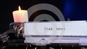 Old typewriter on table, words fake news are printed on paper in large size, candle is burning, retro style, concept of