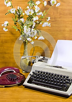 Old typewriter, telephone and ancient vase with camomiles