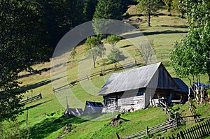 The old Ukrainian hut with a slate roof and a wooden fence in a green fiel