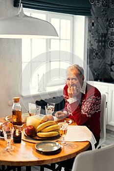 Old unhappy man is sitting at the table