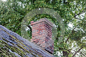 Old unsafe asbestos roof overgrown with moss with chimney