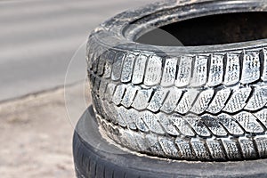 Old used car tires in white paint stacked on top of each other near the tire shop against a blurred background