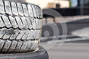 Old used car tires in white paint stacked on top of each other near the tire shop against a blurred background
