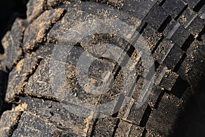 Old used extreme terrain tire with worn wear-resistant tread. Close-up of black muddy off-road tire