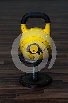 Old and used gym black metal dumbbell with yellow kettlebell on a wooden floor.