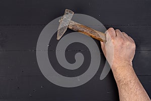 Old used hammer with wooden handle in the male hand above black wooden boards table. DIY concept with copy space above black