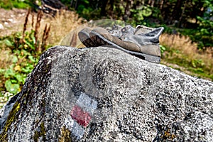 Old used hiking boots and tourist sign on rock