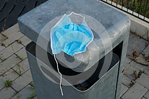 An old and used surgical face mask on a wastebin