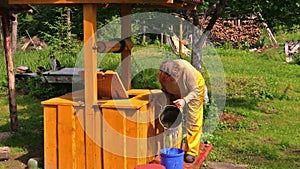 Old villager woman at well, draw water and pour it to bucket