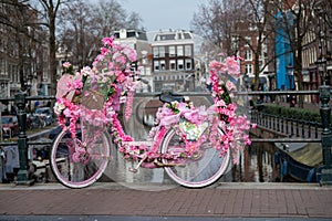 Old vintage bicycle decorated with pink flowers on small bridge in old part of Amsterdam