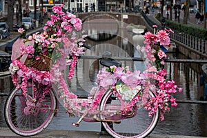 Old vintage bicycle decorated with pink flowers on small bridge in old part of Amsterdam