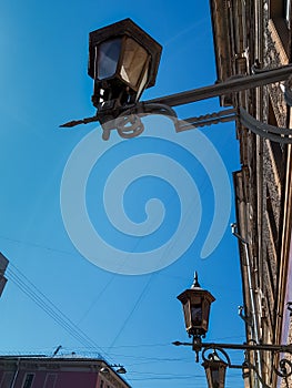 Old vintage black glass street lanterns hanging on wall of beautiful building in of Saint Petersburg in the light of sun. Blue sky