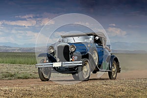 An old vintage blue car traveling on a dusty counrty road on a farm in the Free State of South Africa photo