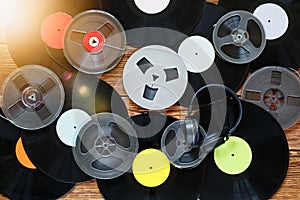 Old vintage bobbins, vinyl records, cassette tapes and headphones on a wood table background. Multicolored labels. Top view. Sun