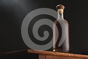 Old vintage bottle of whiskey or brandy, rum or cognac with dust on rustic table, black background. Alcohol drink, no label. Copy