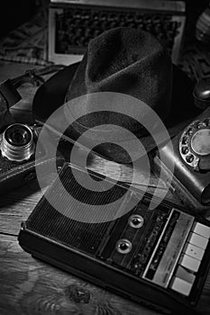 Old vintage cinematic noir scene, detective`s desk with a hat, telephone, camera, portable cassette recorder, and whisky