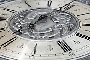 Old vintage clock with metal dial and floral embossed pattern close-up. Black clock hands indicating a time of 6 hours. Beautiful