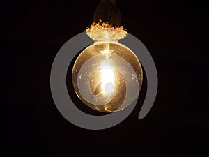 Old vintage dusty edison light bulb hanging on a rope fixture glowing against a black background